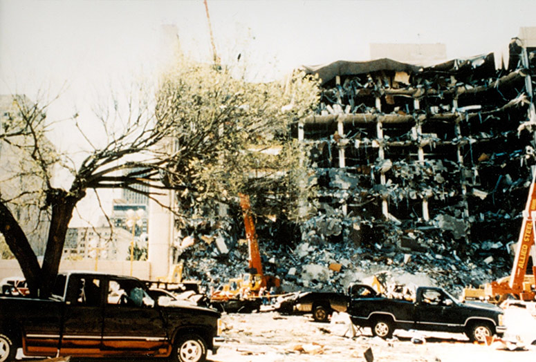 The Survivor Tree stands to the left in the foreground, the destroyed Alfred P. Murrah Federal Building in the background.